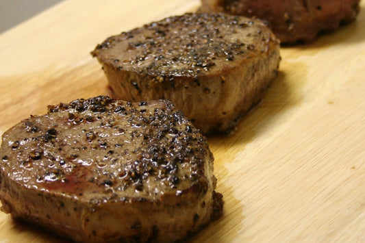 3 cooked fillet steaks with black pepper on a wooden board