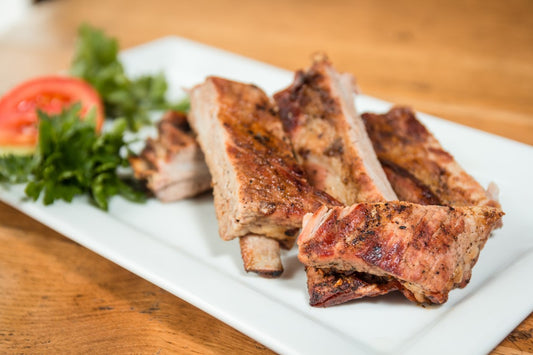 a pile of pork ribs stacked on a white plate with salad leaves