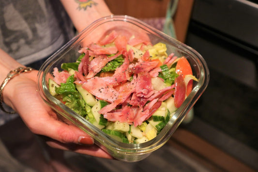 girls hand holding a bowl of salad topped with diced turkey bacon