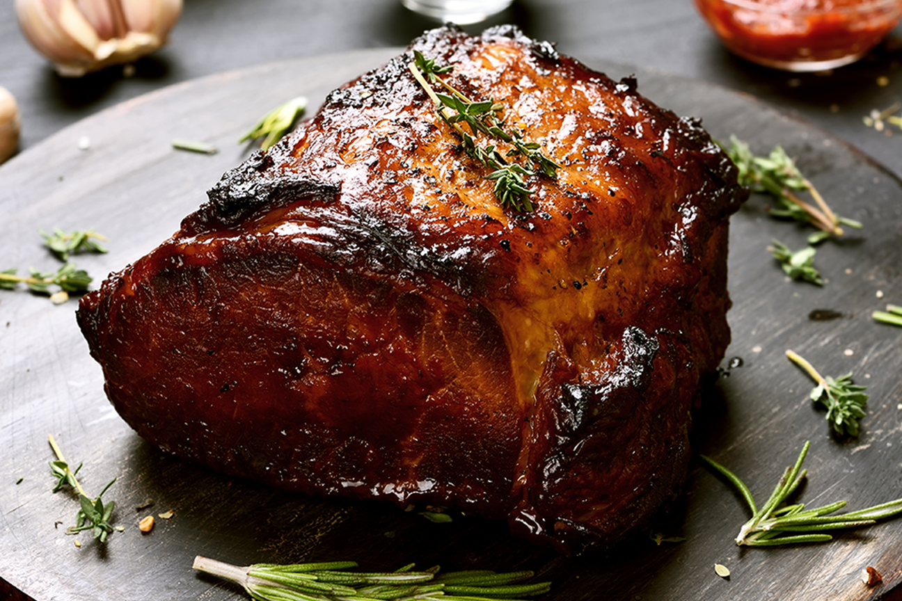 large cooked beef roasting joint resting on a cutting board with herbs