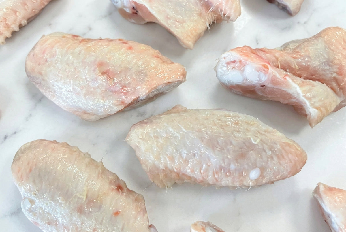 Raw 1 joint chicken wings with skin placed on a dark wooden surface.