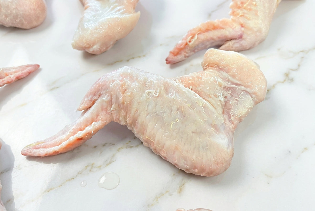Raw 3 joint chicken wings laid out on a dark wooden surface.