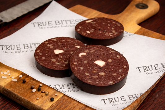 Three slices of black pudding on a wooden cutting board with 'True Bites' paper underneath.