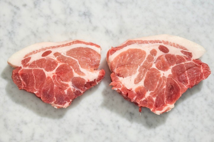 Two raw pork shoulder steak on a marble surface