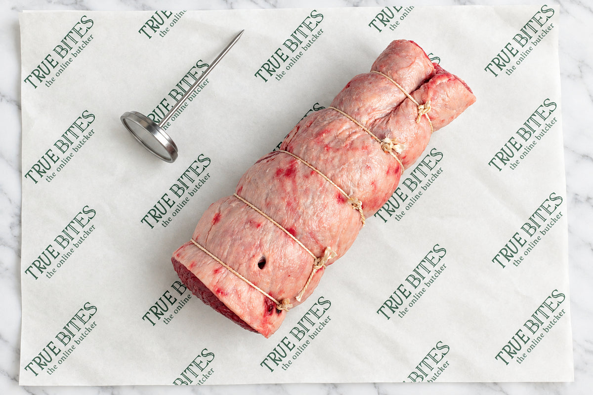 raw rolled and strung beef brisket on branded butcher paper reading 'TRUE BITES'