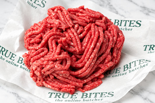 A mound of raw ground beef sits on branded butcher-paper wrapping with the words TRUE BITES butcher visible in green text.