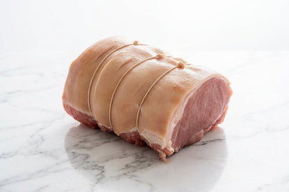 A raw, tied corner gammon roast with rind resting on a white butcher counter.