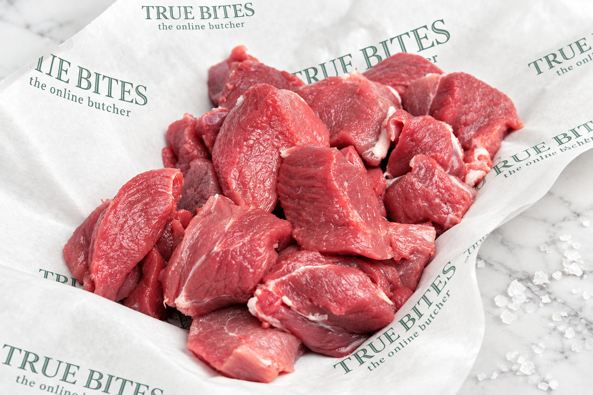 Raw diced lamb leg pieces piled on branded butcher paper over a wooden surface, with coarse salt scattered nearby.