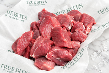 Raw diced lamb leg pieces piled on branded butcher paper over a wooden surface, with coarse salt scattered nearby.