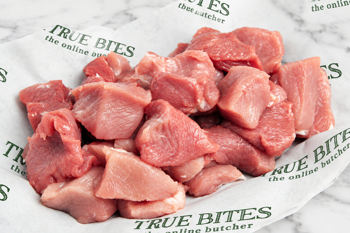 Raw diced pork pieces piled on white butcher paper printed with the brand name 'True Bites'.