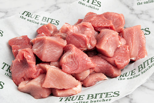 Raw diced pork pieces piled on white butcher paper printed with the brand name 'True Bites'.