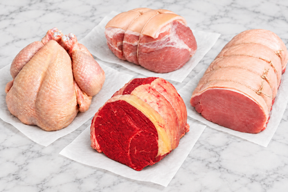 a raw whole chicken, beef joint, pork joint and gammon joint on a marble surface