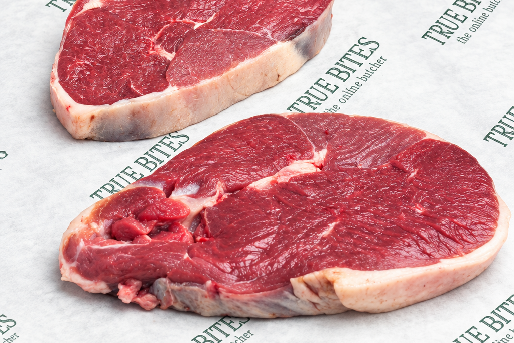Two raw beef chuck roast steaks on branded white butcher paper over a light marble surface. The meat is deep red with visible fat marbling and trim.