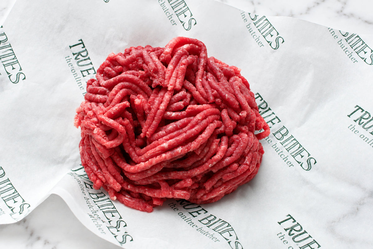 Raw ground beef meat piled on branded white paper packaging with repeated 'TRUE BITES' text, photographed close-up.