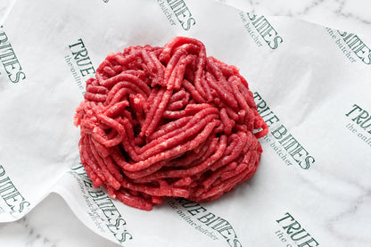 Raw ground beef meat piled on branded white paper packaging with repeated 'TRUE BITES' text, photographed close-up.