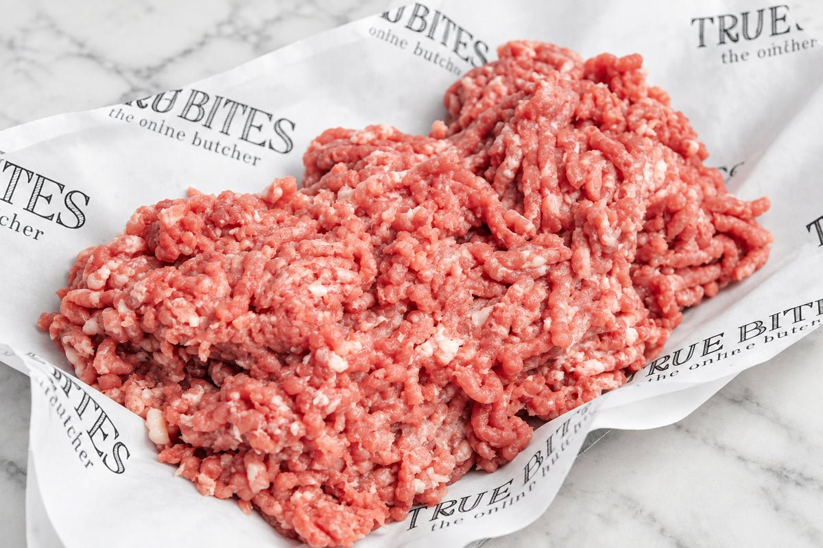Raw ground pork piled on branded butcher paper over a dark wooden surface.