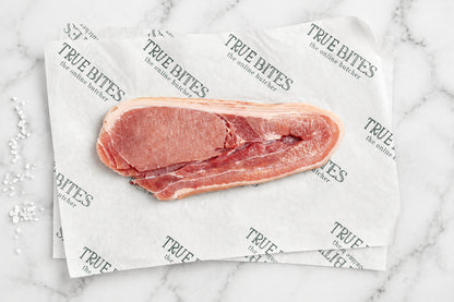 A raw cut of middle bacon with fat layers, placed on branded parchment paper over a dark wooden surface.