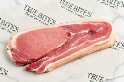A raw cut of middle bacon with visible fat layers, placed on branded butcher paper printed with the brand name TRUE BITES.