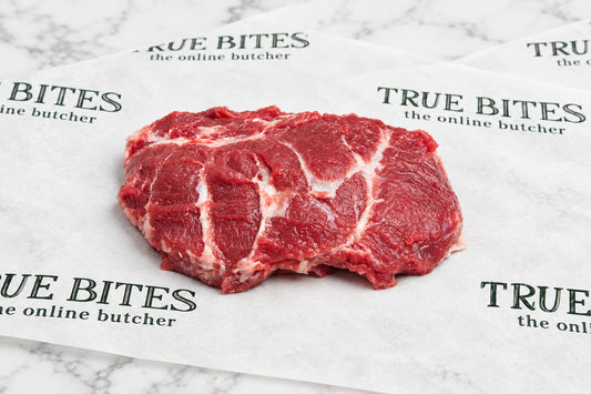 A raw single pigs cheek with white fat marbling, placed on branded butcher paper that reads TRUE BITES the online butcher.