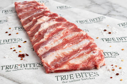 Raw rib rack with visible fat marbling, placed diagonally on branded butcher paper that reads TRUE BITES the online butcher.