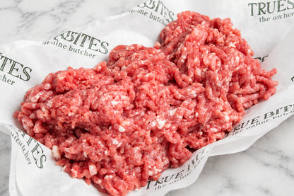 Raw ground pork mince piled on branded butcher paper over a dark wooden surface.