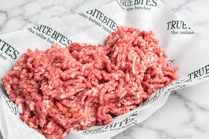 Raw ground pork mince piled on branded butcher paper over a dark wooden surface.