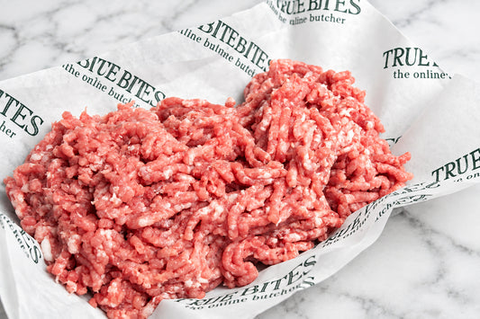 Raw ground pork mince piled on branded butcher paper over a dark wooden surface.