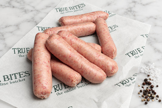 8 raw pork sausages arranged on branded butcher-paper wrapping, with coarse salt and peppercorns on a dark wooden surface.