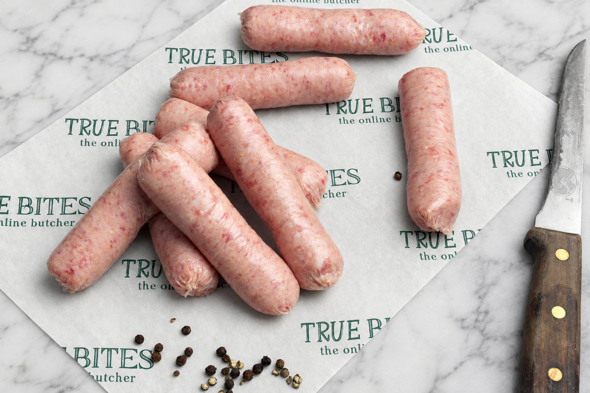 8 raw sausages arranged on branded butcher paper, with a knife at the right and peppercorns on a wooden surface.