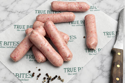 8 raw sausages arranged on branded butcher paper, with a knife at the right and peppercorns on a wooden surface.