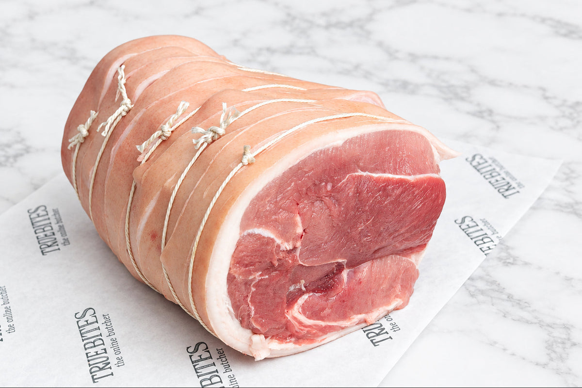 A tied raw pork shoulder roast resting on branded butcher paper reading 'TRUE BITES the online butcher' over a dark countertop.