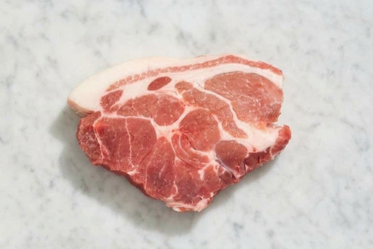 A raw cut of pork shoulder with visible marbling and a layer of white fat, placed on a light gray marble surface.