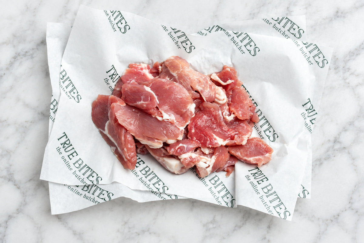 Raw bacon misshapes on branded white paper over a dark wooden surface. The paper is printed repeatedly with the brand name 'TRUE BITES'.