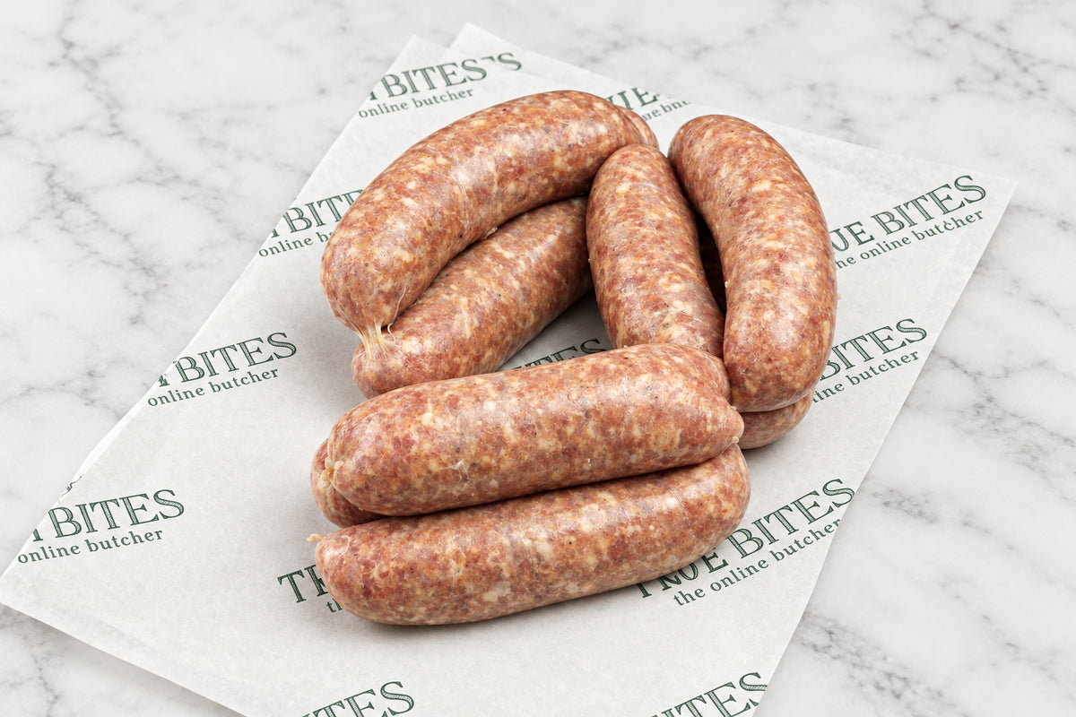 Several raw sausages arranged on branded butcher paper over a dark wooden surface, with a few red chili peppers and coarse salt/spice scattered nearby.