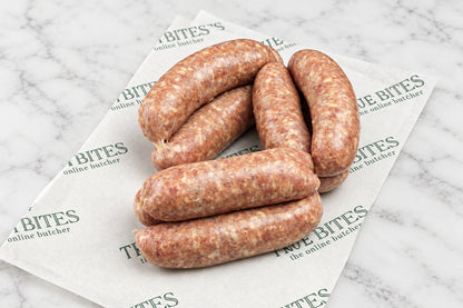 Several raw sausages arranged on branded butcher paper over a dark wooden surface, with a few red chili peppers and coarse salt/spice scattered nearby.