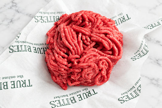 A ball of textured ground beef meat on branded True Bites paper wrapper, set on a dark wooden surface.