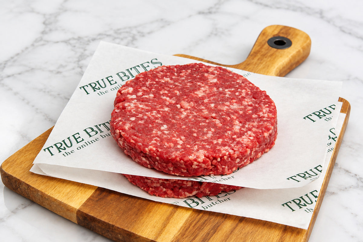 2 raw gourmet steak burgers separated by branded true bites butcher paper on a wooden cutting board