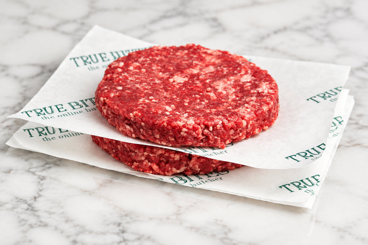 2 raw gourmet steak burgers on wooden cutting board separated by branded TRUE BITES butcher paper