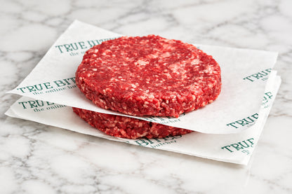 2 raw gourmet steak burgers on wooden cutting board separated by branded TRUE BITES butcher paper