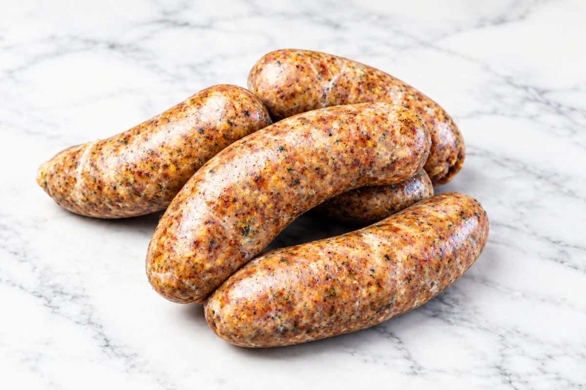 Four links of raw jerk chicken sausage stacked on a dark wooden cutting board.