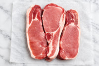 Sliced raw back bacon with visible fat marbling, arranged side by side on branded butcher paper.