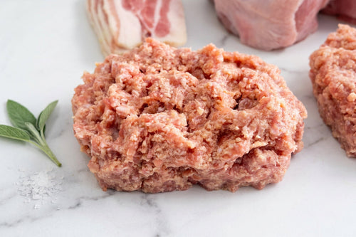 450g raw pork sausage meat on a white surface with other meats in the background