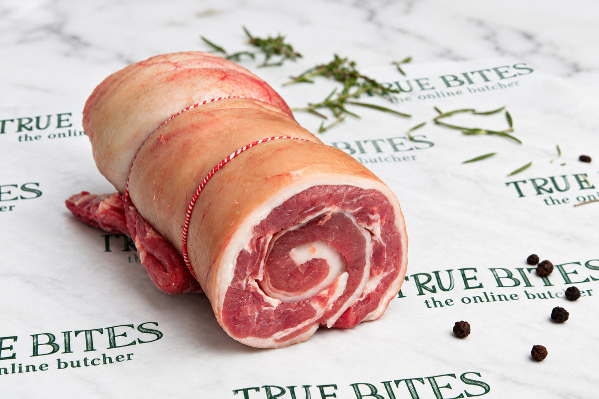 A rolled piece of lamb breast meat tied with a red string, resting on branded butcher paper with scattered peppercorns.