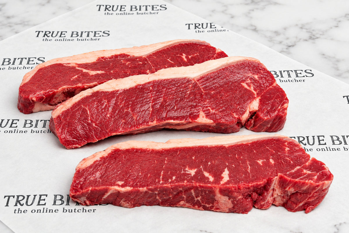 Three raw beef sirloin steaks with visible marbling and fat layers, arranged on branded butcher paper over a dark wooden surface.