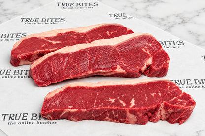 Three raw beef sirloin steaks with visible marbling and fat layers, arranged on branded butcher paper over a dark wooden surface.