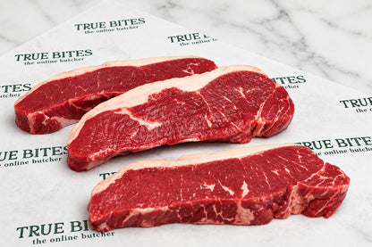 Three raw beef sirloin steaks with marbling and fat layers, arranged on white butcher paper printed with the brand name 'TRUE BITES'.