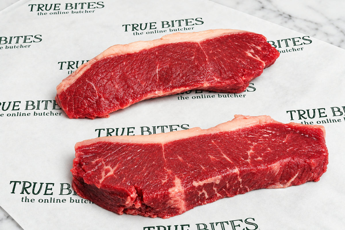 Two raw beef sirloin steaks with white fat marbling, placed on white butcher paper printed with the brand name 'True Bites'.
