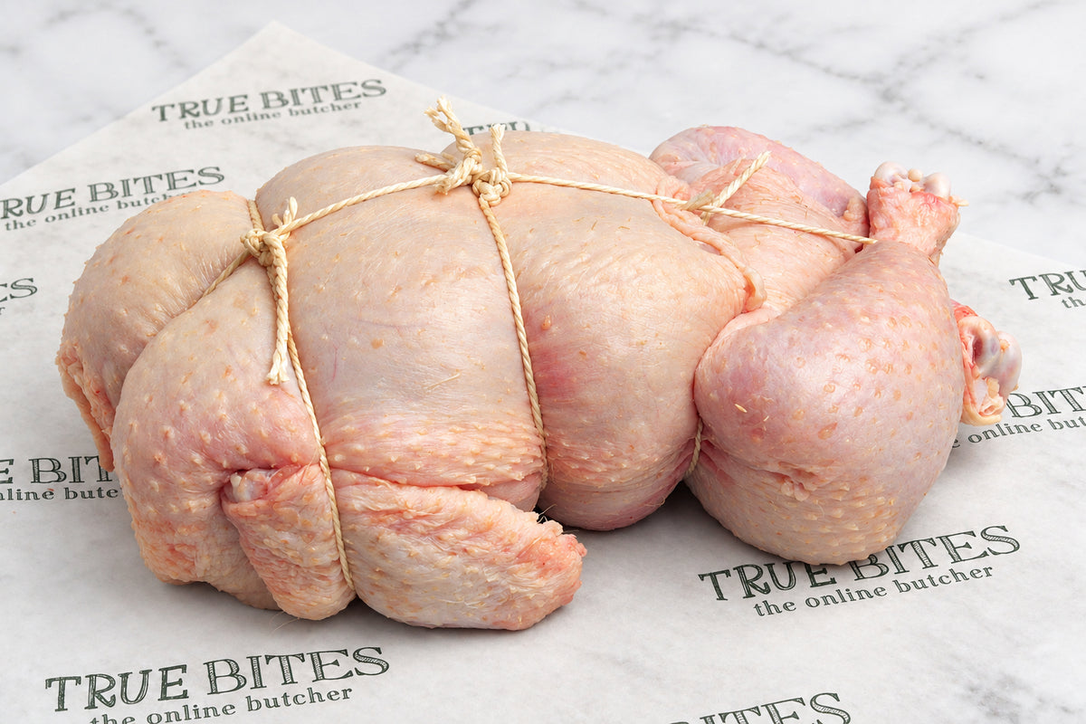 A raw, whole spatchcock chicken tied with string, placed on branded butcher paper that reads TRUE BITES the online butcher.