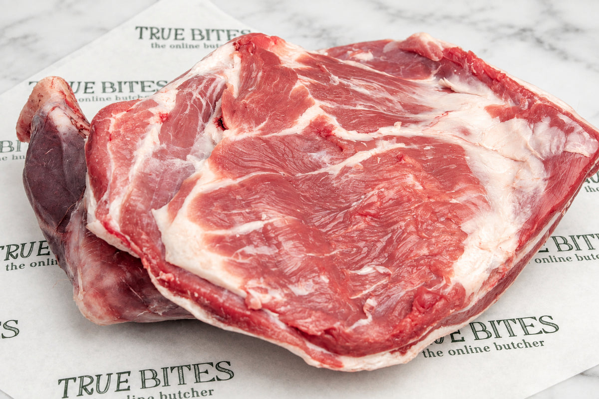 A close-up of a whole lamb shoulder with white fat, resting on printed butcher paper branded TRUE BITES.