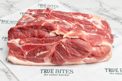 A raw whole pork butt with white fat layers, placed on branded butcher paper over a dark wooden surface. The paper shows the visible brand name TRUE BITES.